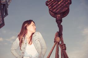 Posing model girl, near the crane in the port, at colorful sky with clouds on background