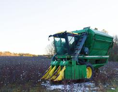 Green and yellow "John Deere" tractor machine, on the field, with snow, near the colorful trees