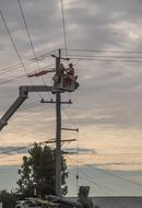 Workers, repairing electricity on the power poles, on the cherry picker, at colorful sunset in the sky with clouds