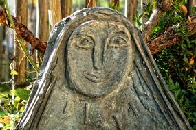 Beautiful sculpture with the face, among the colorful plants, in light
