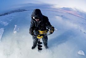 Man, cutting hole in the beautiful, frozen lake, with auger, in winter