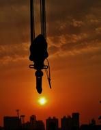 Silhouette of a crane hook at beautiful and colorful background with sunset and city