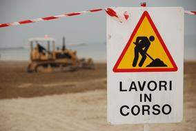 Colorful "Work In Progress" sign, and machine, near the sea