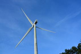 Wind turbine, near the trees, under the beautiful blue sky with clouds