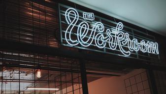 Beautiful, white neon "The Workroom" sign on the black fence