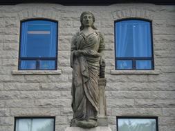 Beautiful statue of the woman, near the building, with the windows, with reflections