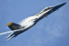 Beautiful, flying, blue and yellow plane of the "Blue Angels" with white contrail, at blue sky with white clouds on background