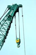 Close-up of the green crane with the colorful hook at blue sky background