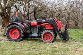 Red and black tractor on the green meadow among the trees