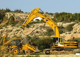Yellow heavy machines, on the yellow rocks with green plants, on the beautiful landscape