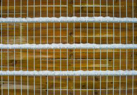 Brown wooden wall behind the metal fence with snow