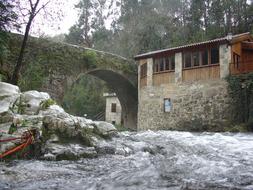 Beautiful landscape of the stone bridge and building near the river among the green trees in Galicia, Spain