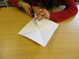 Female, cutting white paper with scissors, on the wooden table