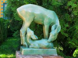 Beautiful, shiny, green and yellow statue of the deer and fawn, near the green plants