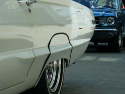 Beautiful, shiny, white, vintage Mustang car, near the other car, on the road