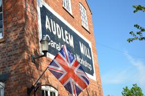 British flag on the Audlem Mill, among the green trees, at blue sky and white clouds on background, in England, UK