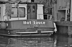 Black and white photo with the retro boat, with "Hot Sauce" sign, on the water, with the ripple