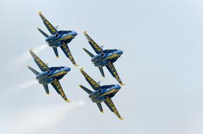 Flying, blue and yellow planes of the "Blue Angels", with white contrails, in the sky