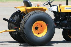 Yellow vehicle with the black and yellow wheels and towbar, in light, with the shadow