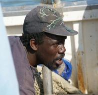 African fisherman with the beard, in cap, on the boat, in sunlight