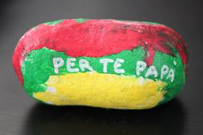 Red, green and yellow, painted stone with the "Per Te Papa" sign, with shadow