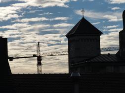 Silhouettes of the crane, behind the church, with the steeple with cross, at blue sky with clouds on background, in Ulm, Germany