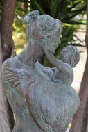 Statue of the mother with the child, near the green plants, in Italy