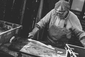 old man cuts fish on wooden table