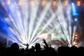 Silhouettes of the crowd, near the colorful stage with lights and smoke on the concert