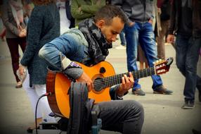 Musician, playing on the wooden guitar, on the street, among the people