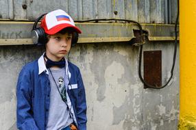 Portrait of a boy in cap with Russian flag and headphones, near the wall