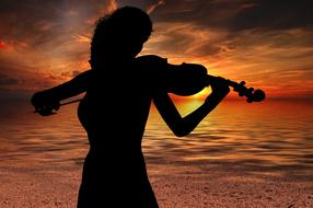 black silhouette of a violin player on the beach at dusk