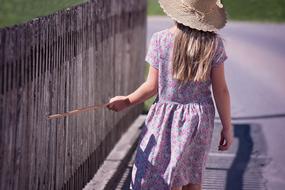 child girl walks away along wooden fence