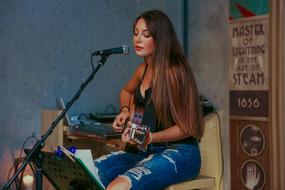 Girl in ripped jeans, playing on the guitar and singing with the microphone