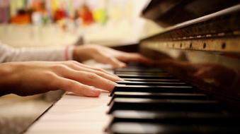 Hands, playing on the shiny, white and black keys of the piano, at blurred background