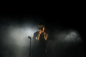 Man in glasses, with the microphone, on the stage, among the smoke and darkness, in light