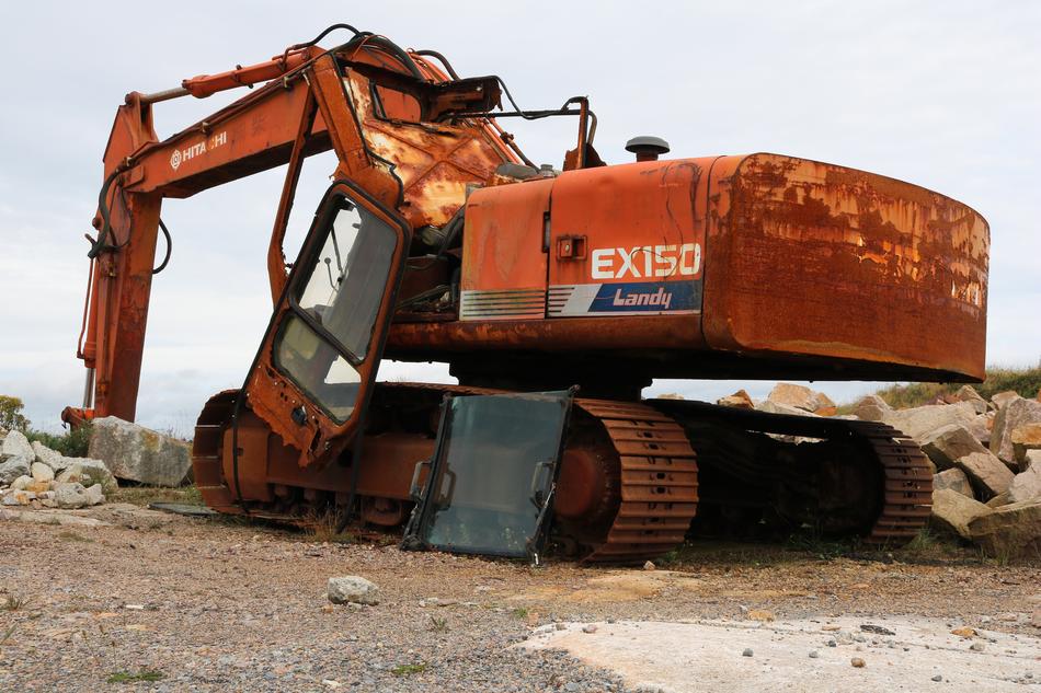Old, rusted, orange excavator on the site with rocks, at cloudy sky on background