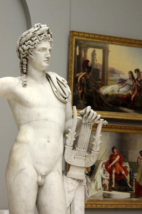 Beautiful white statue of the man with wreath and musical instrument, near the colorful paintings, in the museum in France