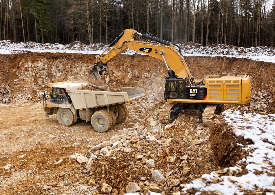 Yellow and black 'Cat 390f' excavator and truck in the pit, among the trees