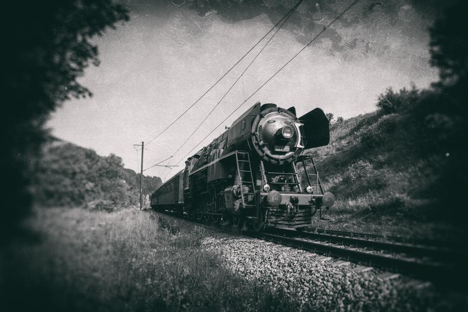Black and white photo of the beautiful train on the railways, among the hills, on the beautiful landscape