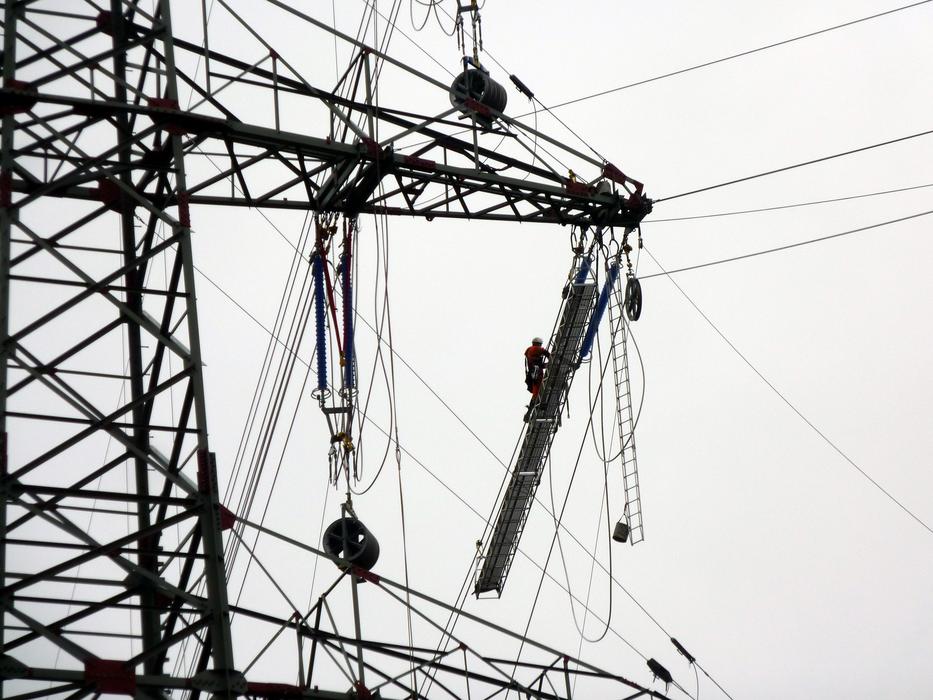 Black and white photo with the close-up of a tower of the power lines, at cloudy sky on background