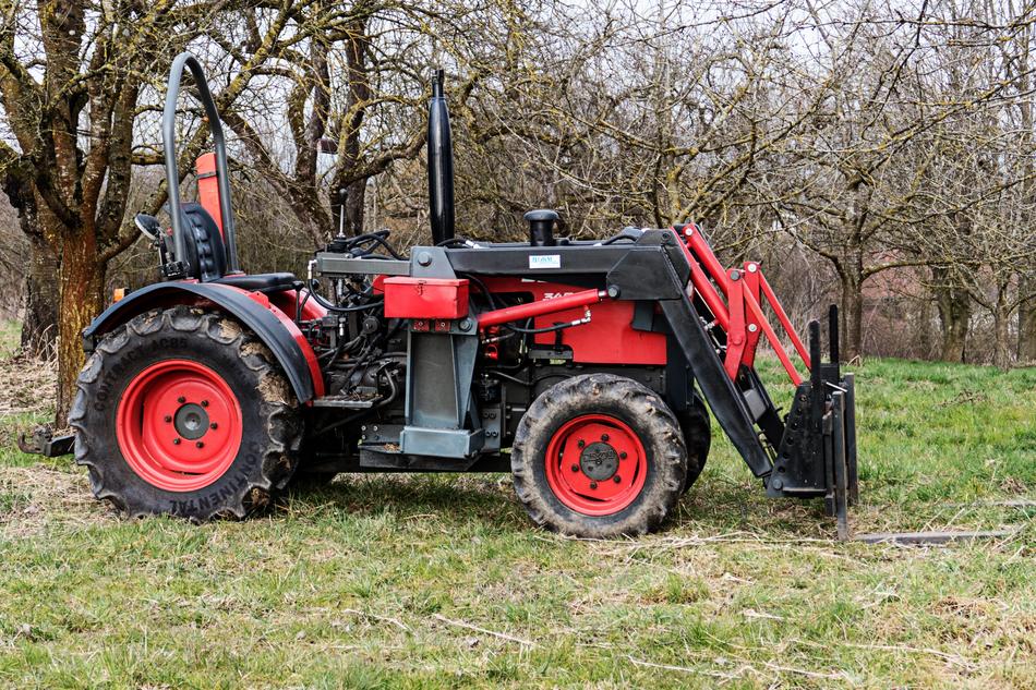 Red and black tractor on the green meadow among the trees
