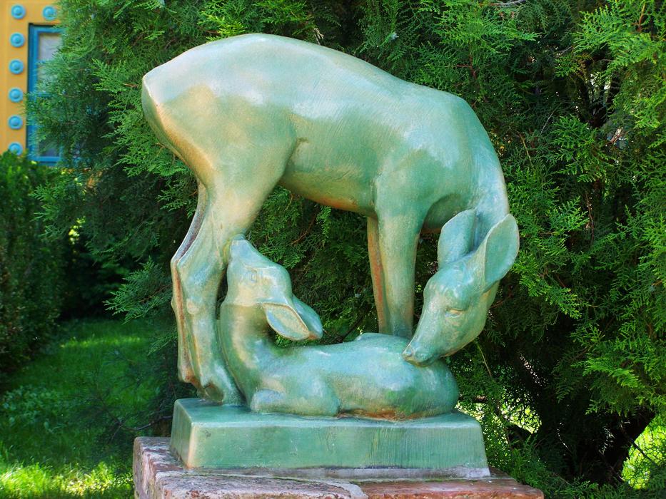 Beautiful, shiny, green and yellow statue of the deer and fawn, near the green plants