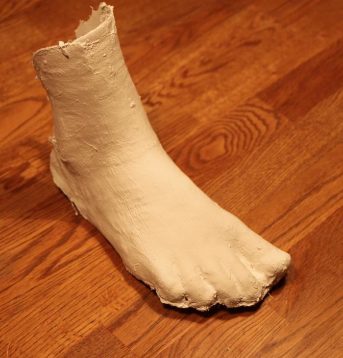 Human foot of the statue, on the wooden surface