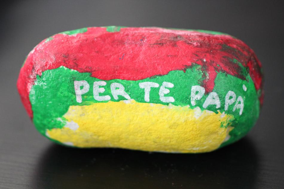 Red, green and yellow, painted stone with the 'Per Te Papa' sign, with shadow