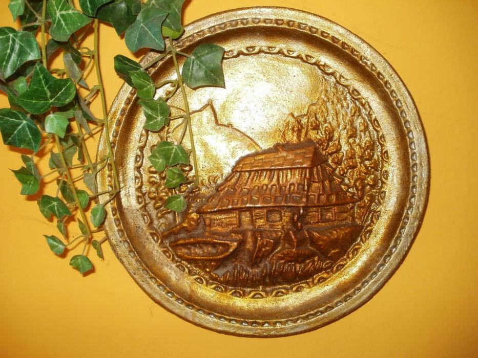 Beautiful, shiny gold plate with the landscape with the hut, and green plant with leaves