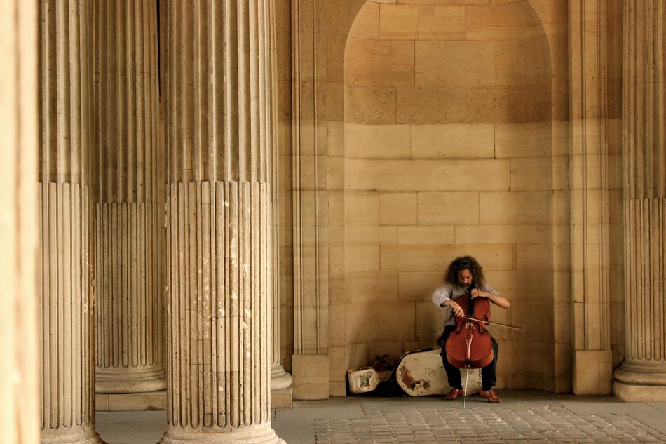Person playing on the cello near the beautiful building with columns in Paris, France
