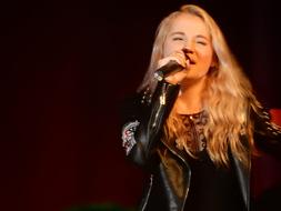 Blonde singer woman with microphone, singing on the concert