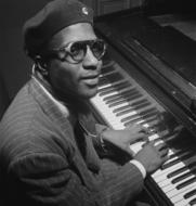 Black and white portrait of Thelonious Sphere Monk in glasses and hat, playing on the piano