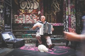 Street performer, playing on the accordion, with the cute and beautiful, white dog, among the colorful graffities